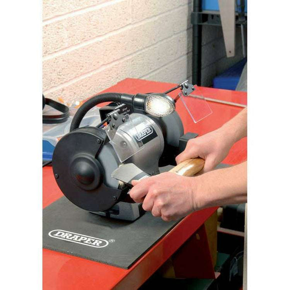 Draper 6" 370W bench grinder in grey with black guards, work light and grinding wheel sharpening a tool