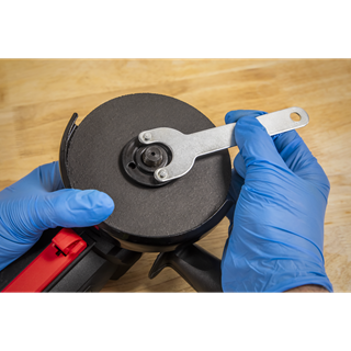 Sealey 115mm angle grinder with black disc, red handle and silver spindle wrench being adjusted